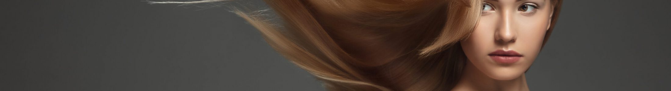 Beautiful model with long smooth, flying blonde hair isolated on dark grey studio background. Young caucasian model with well-kept skin and hair blowing on air. Concept of salon care, beauty, fashion.